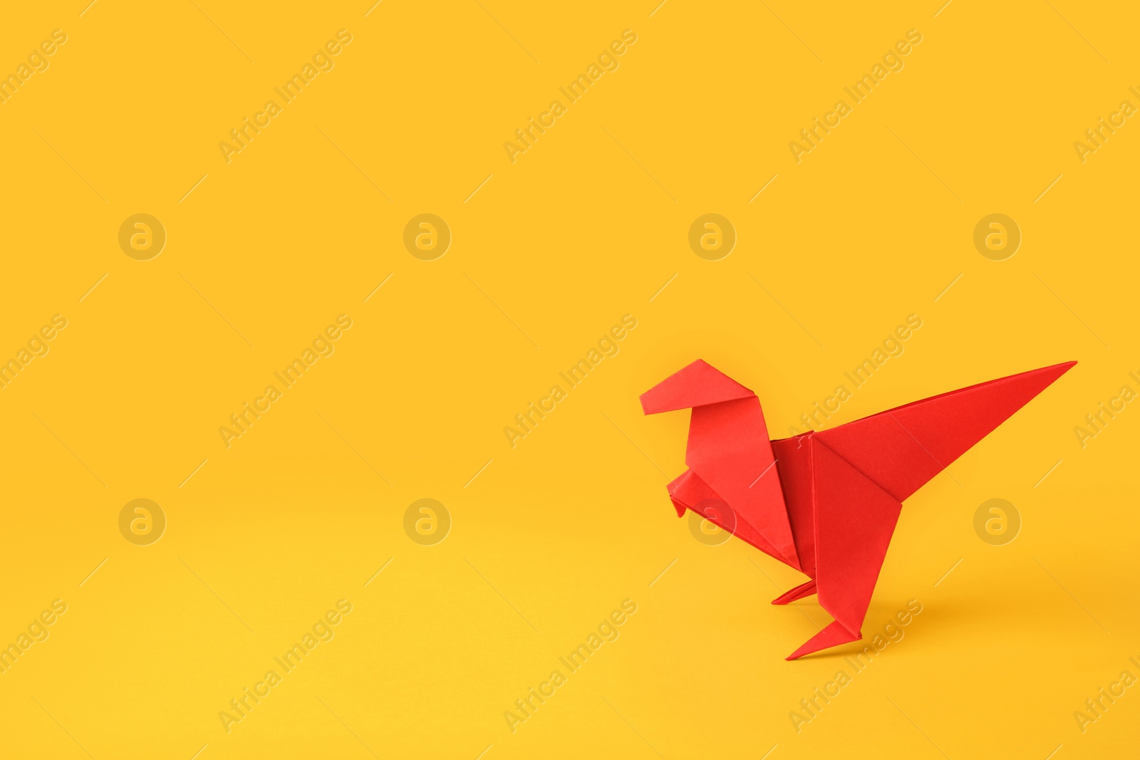 Photo of Origami art. Handmade red paper dinosaur on yellow background, space for text