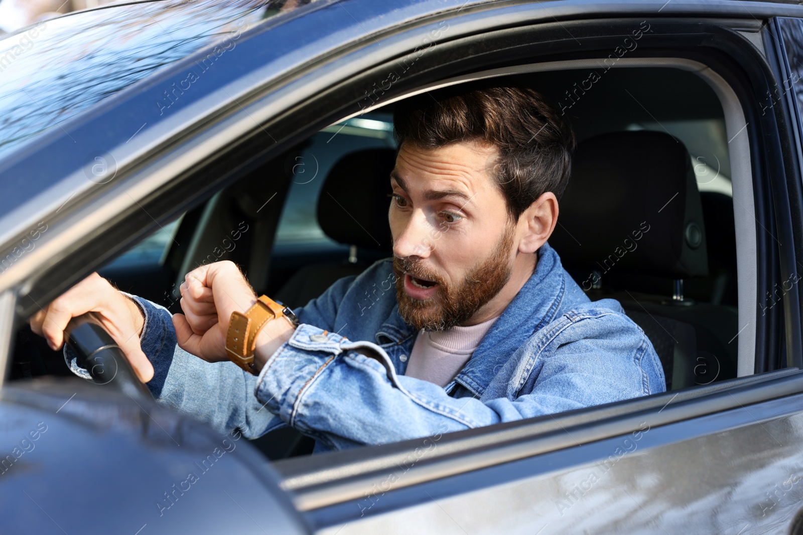 Photo of Emotional man checking time on watch in car. Being late concept