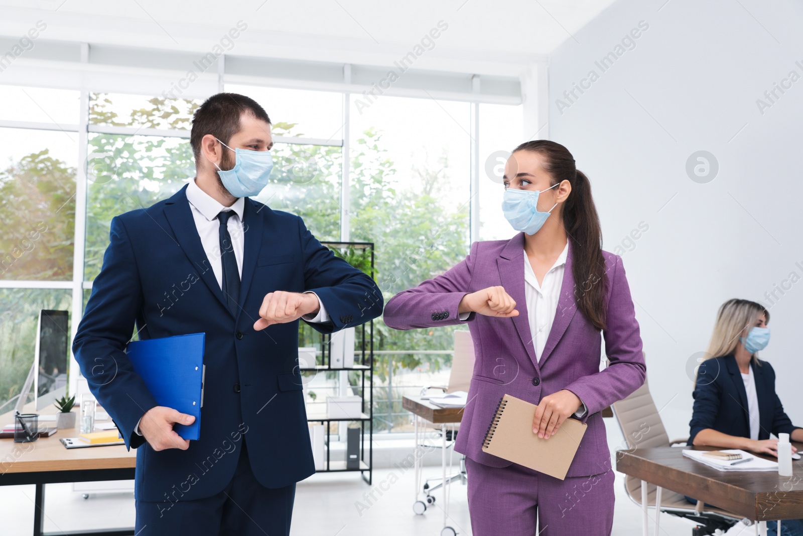 Photo of Office employees in masks greeting each other by bumping elbows at workplace