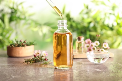 Photo of Dripping natural tea tree essential oil into bottle on table