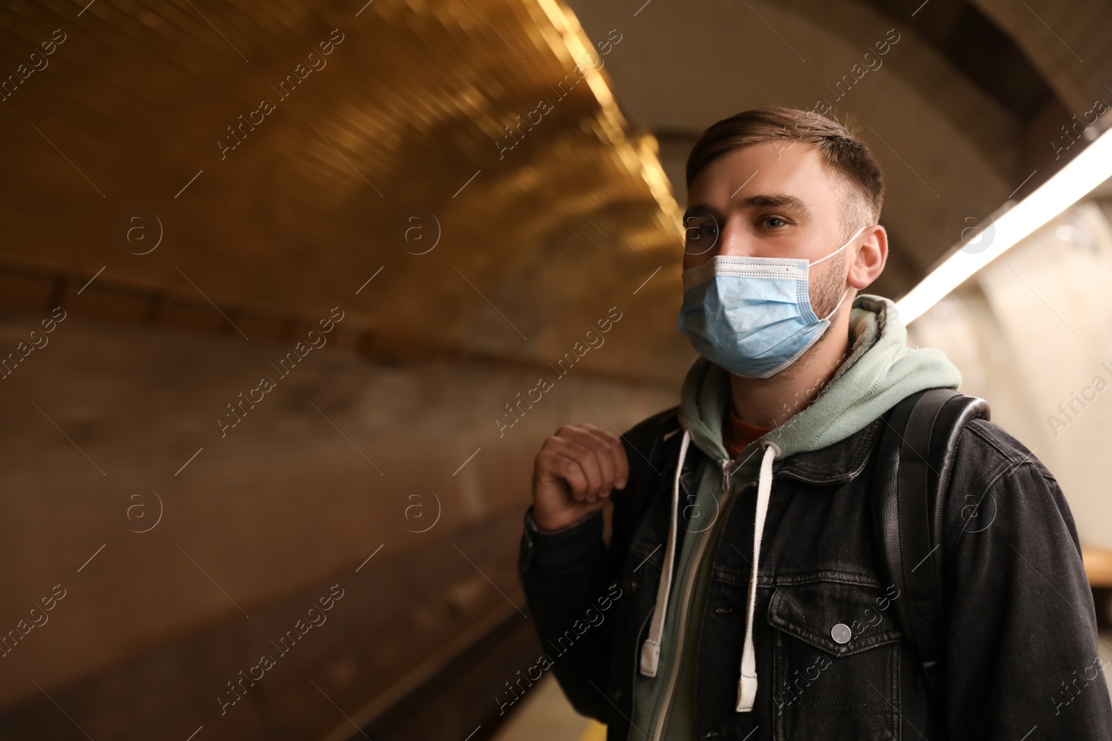 Photo of Young man in protective mask at subway station, space for text. Public transport