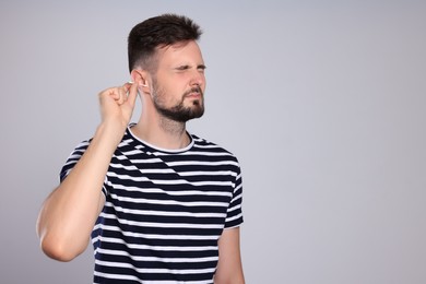 Young man cleaning ear with cotton swab on light grey background. Space for text