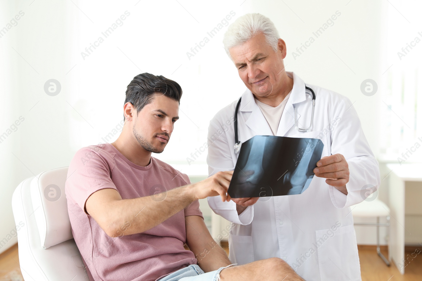 Photo of Senior doctor with X-ray and young patient in clinic. Knee problem