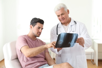 Photo of Senior doctor with X-ray and young patient in clinic. Knee problem