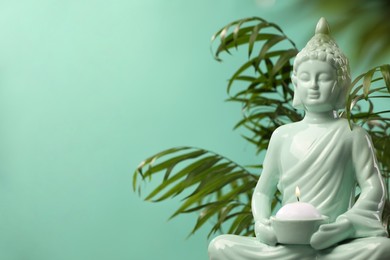 Buddhism religion. Decorative Buddha statue with burning candle and houseplant against turquoise wall, space for text