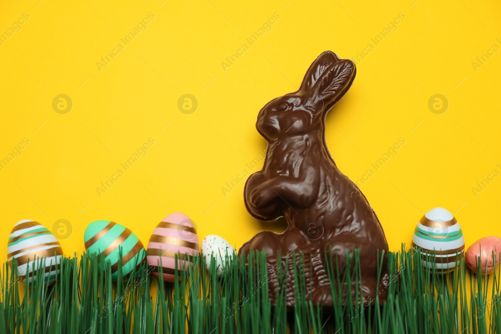 Photo of Chocolate Easter bunny and eggs with green grass on yellow background. Space for text