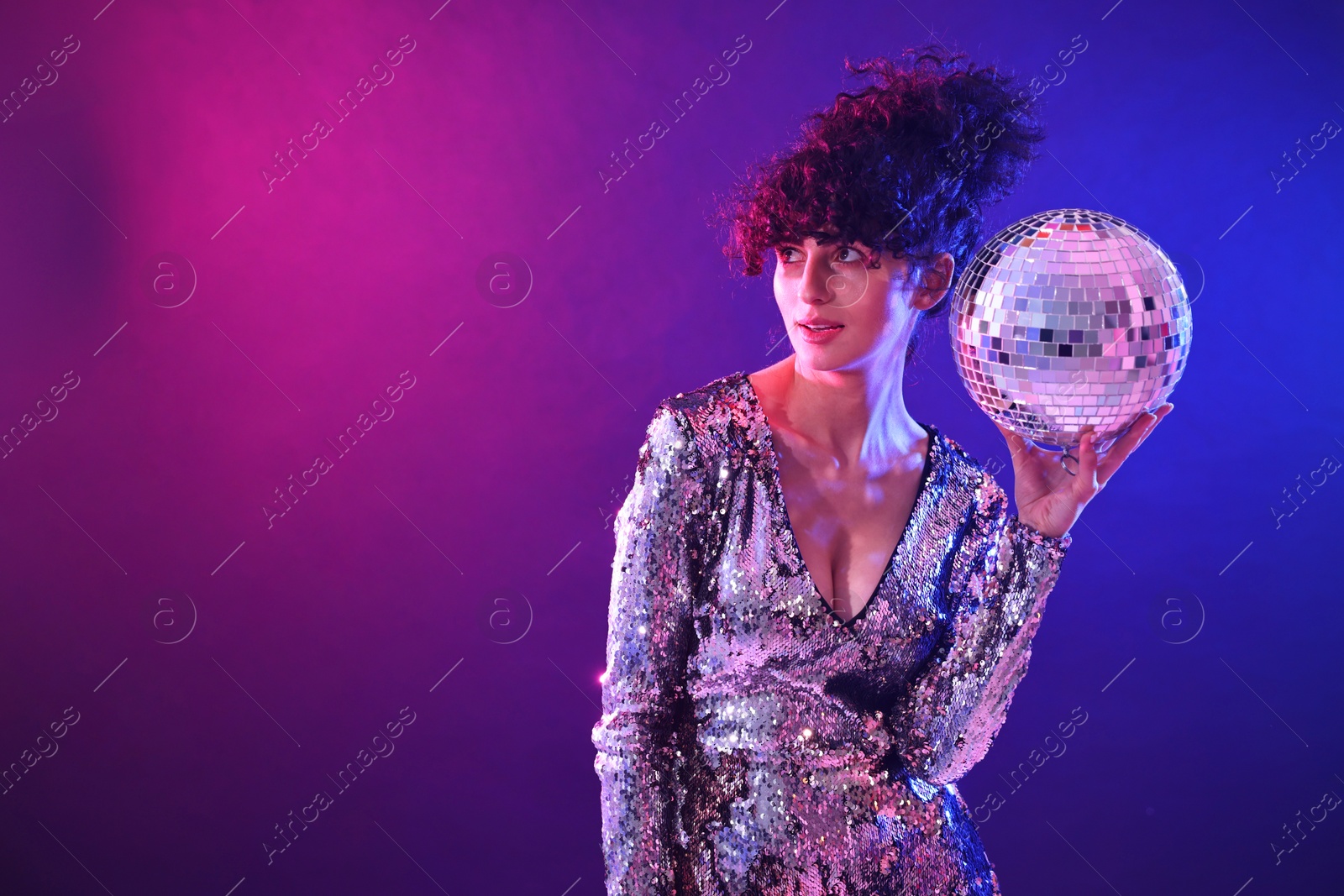 Photo of Beautiful young woman with disco ball posing on color background in neon lights. Space for text