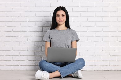 Photo of Student with laptop sitting on floor near white brick wall