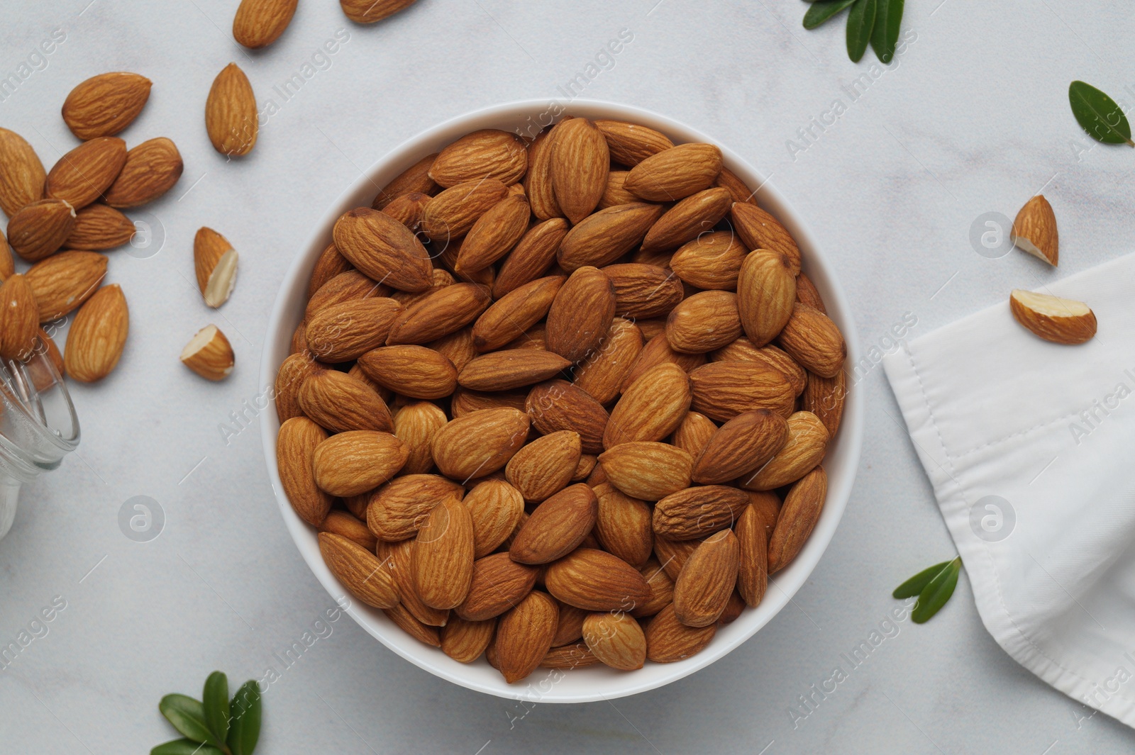 Photo of Bowl with delicious almonds and fresh leaves on white marble table, flat lay