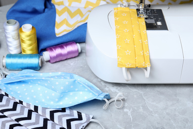 Photo of Sewing machine, homemade protective masks and threads on grey marble table