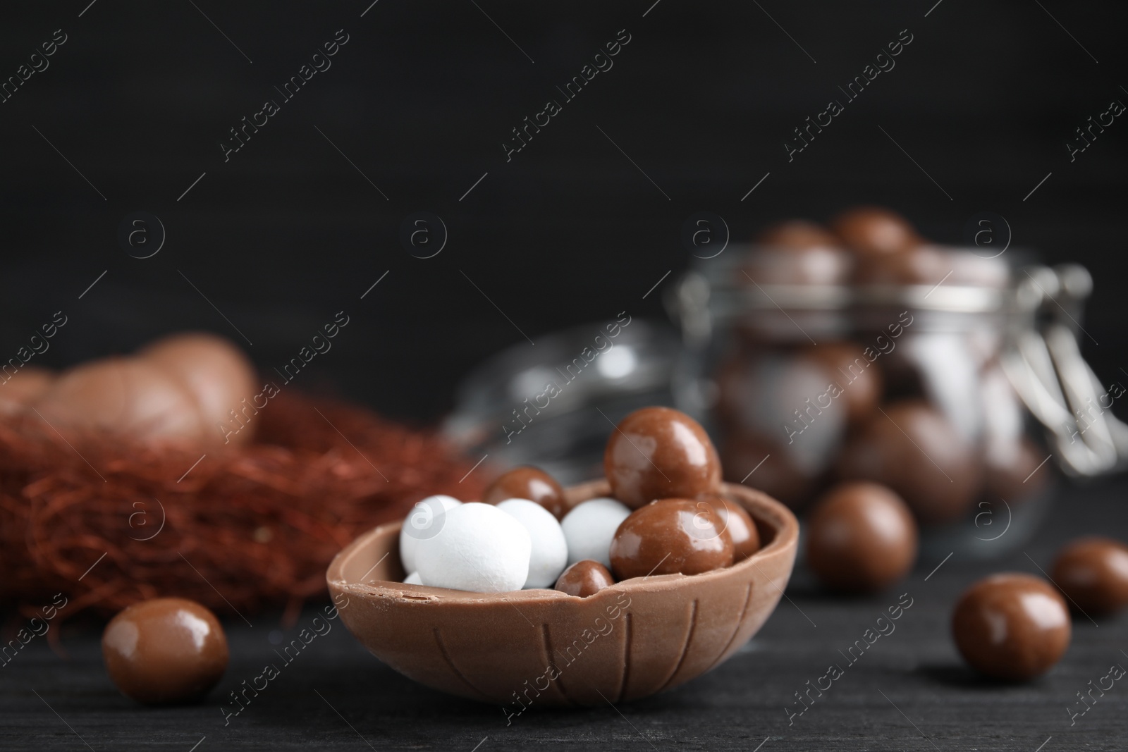 Photo of Half of tasty chocolate egg with candies on black wooden table, space for text