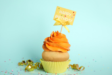 Photo of Beautiful birthday cupcake, streamers and confetti on light blue background