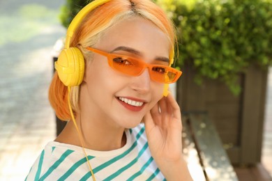 Photo of Beautiful young woman with bright dyed hair listening music outdoors