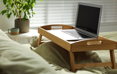 Photo of Wooden tray with modern laptop on bed indoors