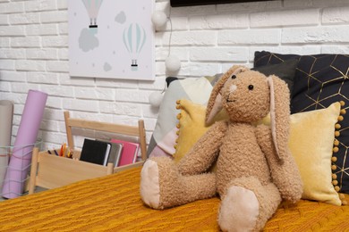 Photo of Cute toy bunny on bed with orange blanket. Bedroom interior