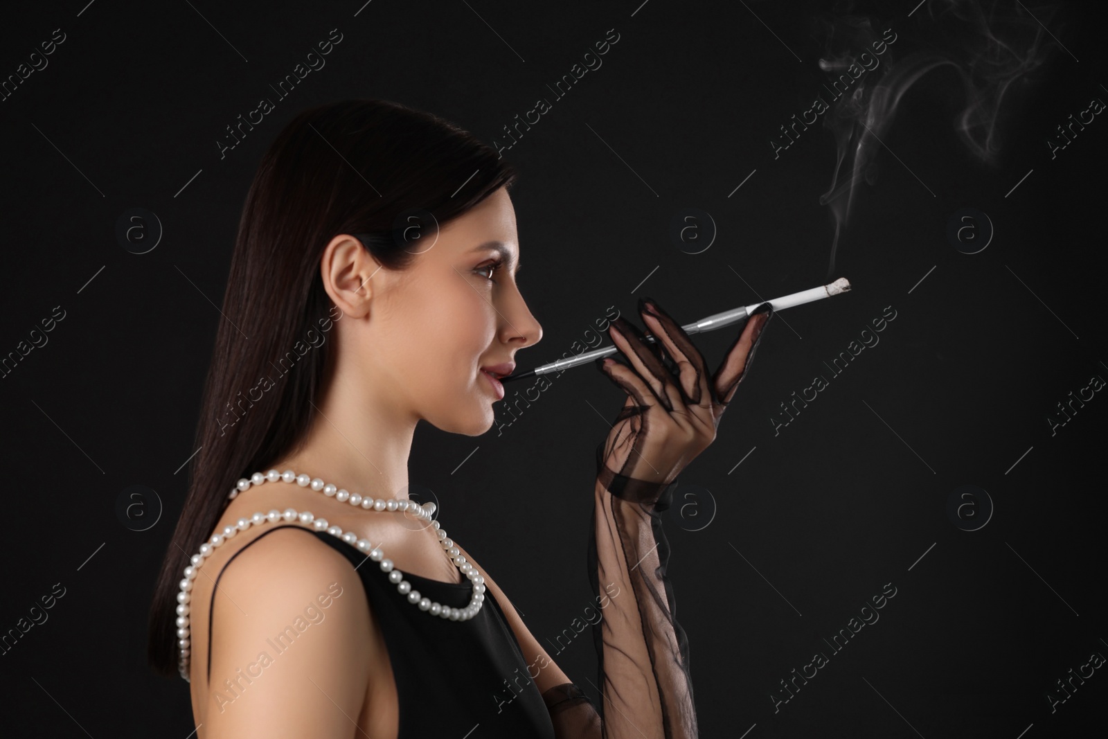 Photo of Woman using long cigarette holder for smoking on black background, space for text