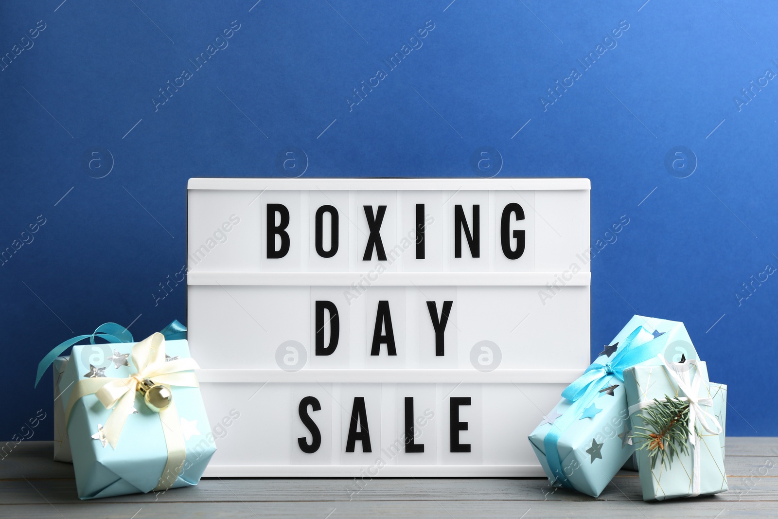 Photo of Composition with Boxing Day Sale sign and Christmas gifts on white table against blue background