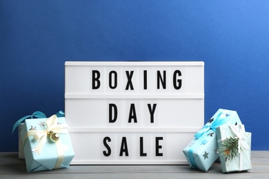 Composition with Boxing Day Sale sign and Christmas gifts on white table against blue background