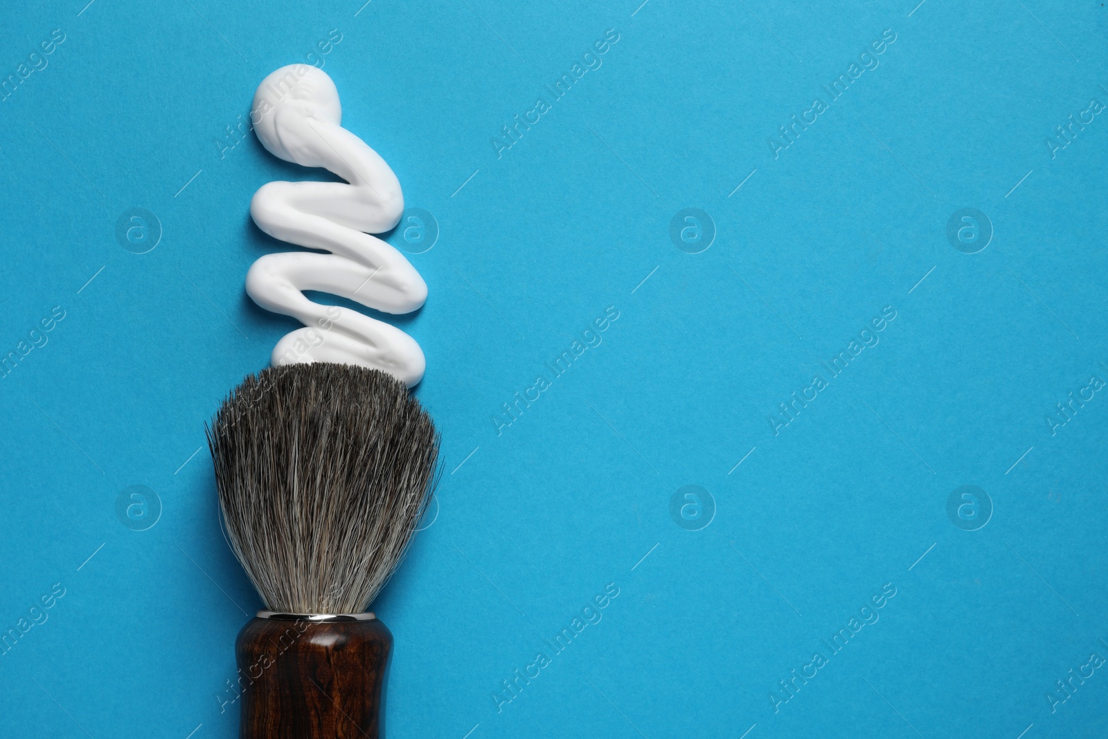 Photo of Brush and sample of shaving foam on blue background, top view. Space for text