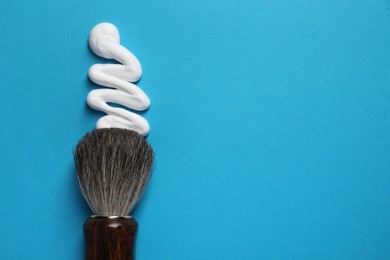 Photo of Brush and sample of shaving foam on blue background, top view. Space for text
