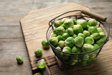 Photo of Metal basket with fresh Brussels sprouts on wooden table. Space for text