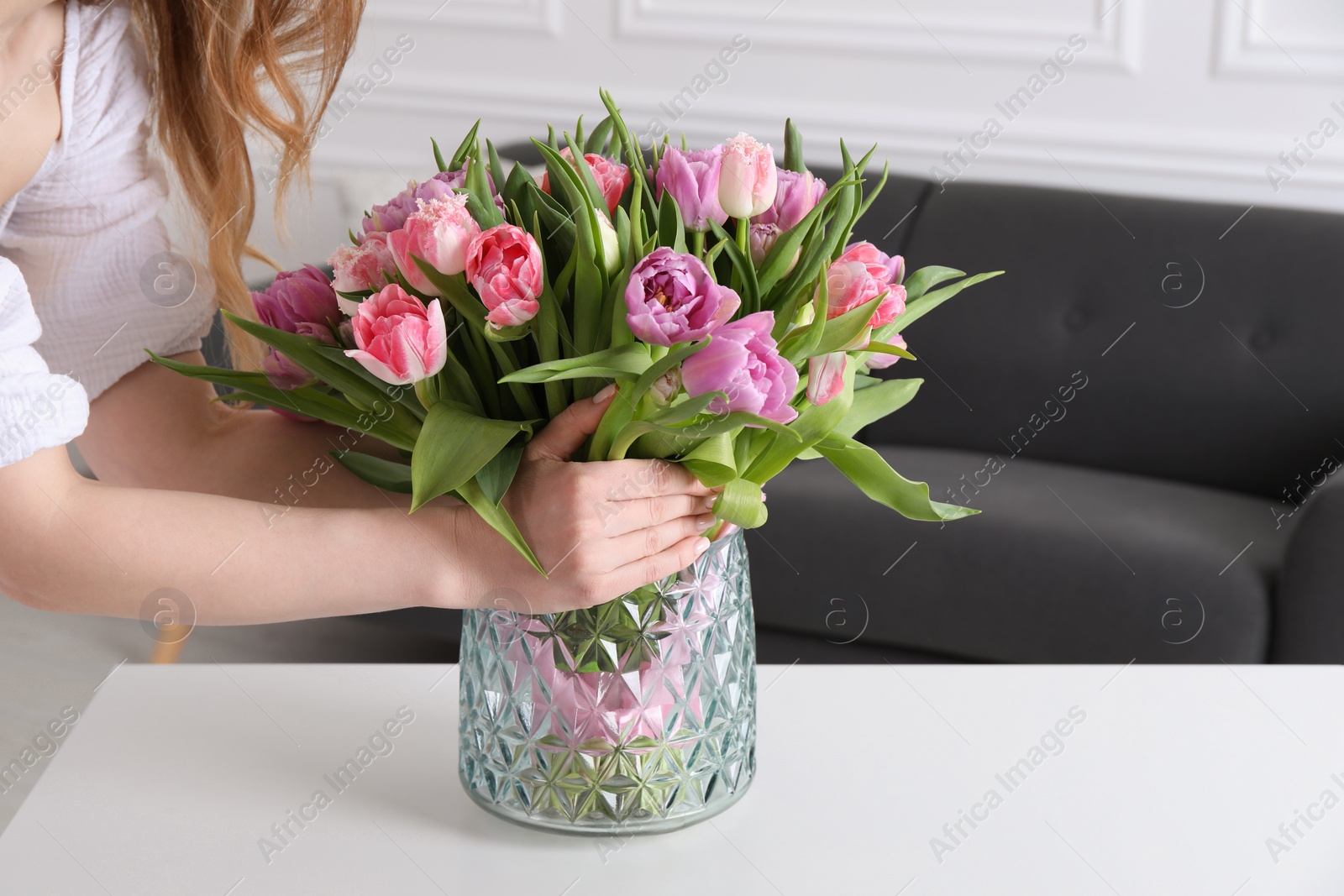 Photo of Woman putting bouquet of beautiful tulips in vase indoors, closeup. Space for text