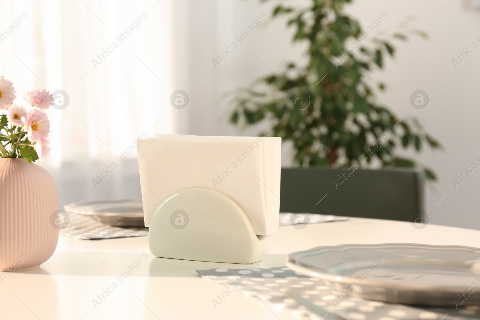 Photo of Ceramic napkin holder with paper serviettes on table indoors