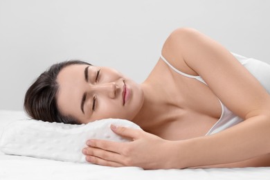 Woman sleeping on orthopedic pillow against light grey background