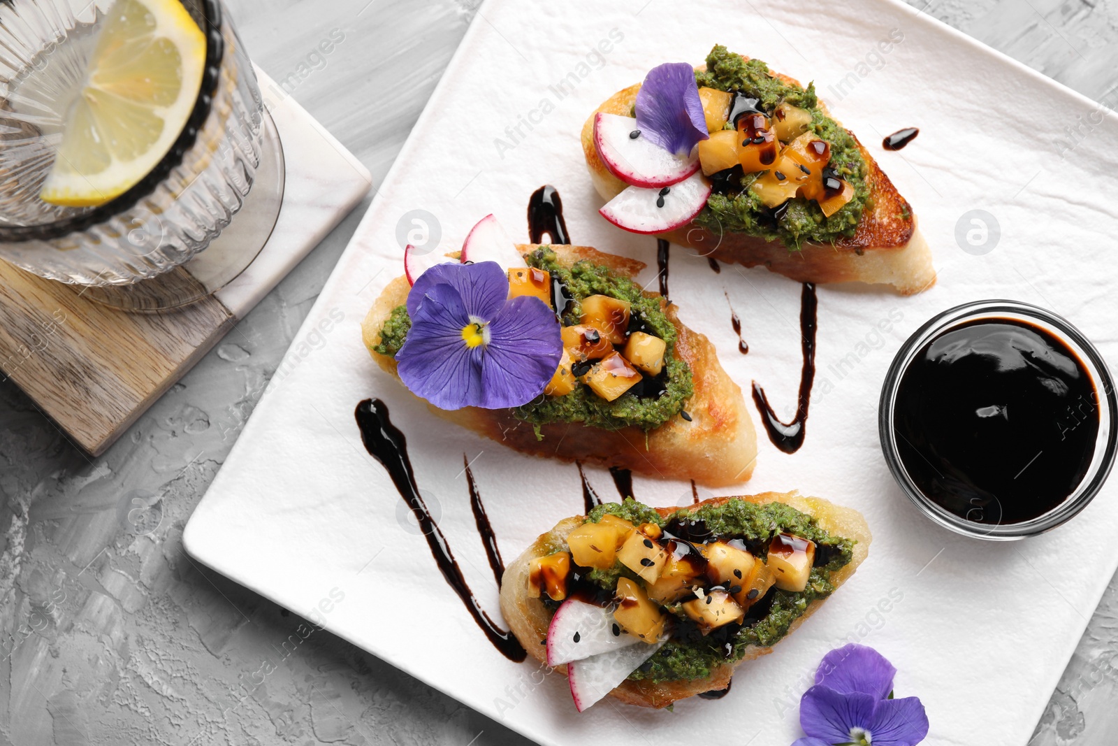 Photo of Delicious bruschettas with pesto sauce, tomatoes and balsamic vinegar served on gray textured table, flat lay