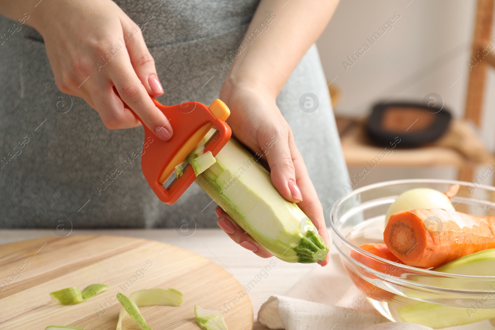 Photo of Woman peeling fresh zucchini at table indoors, closeup