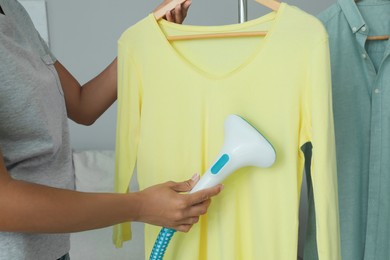 Photo of Woman steaming shirt on hanger at home, closeup