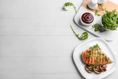 Tasty grilled chicken fillet with sauce, mushrooms and arugula on white wooden table, flat lay. Space for text