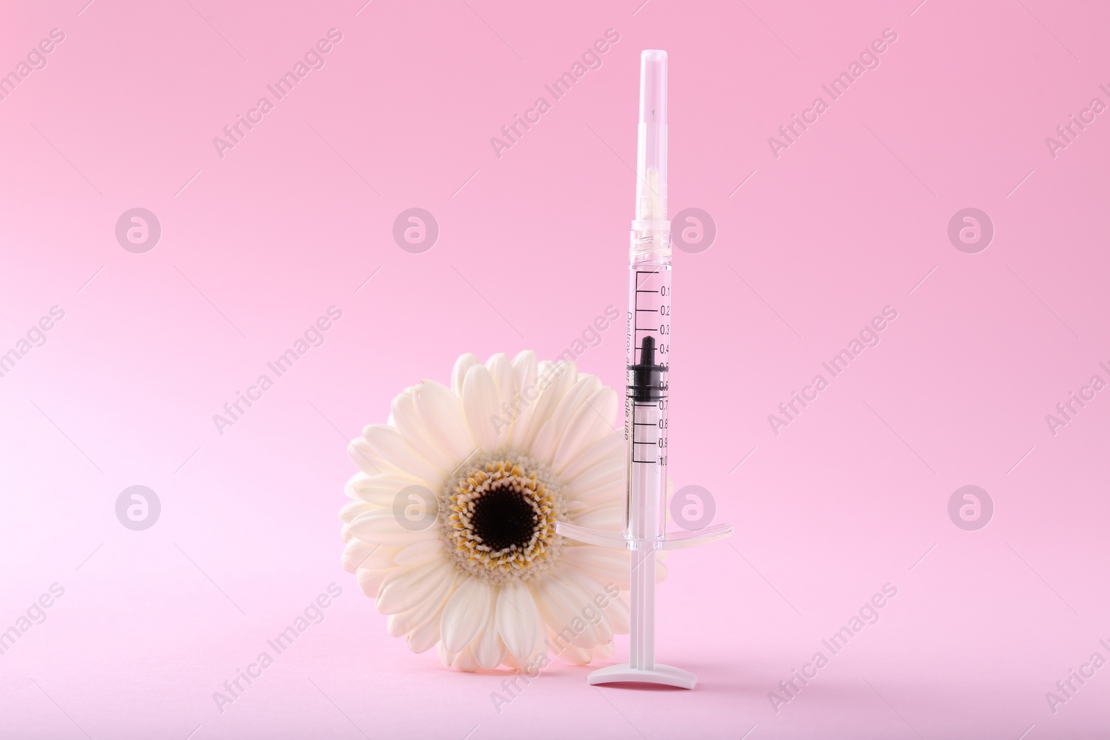 Photo of Cosmetology. Medical syringe and gerbera flower on pink background