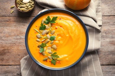 Photo of Delicious pumpkin cream soup in bowl on wooden background, top view