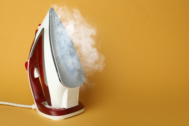 Image of Modern iron with steam on orange background, space for text