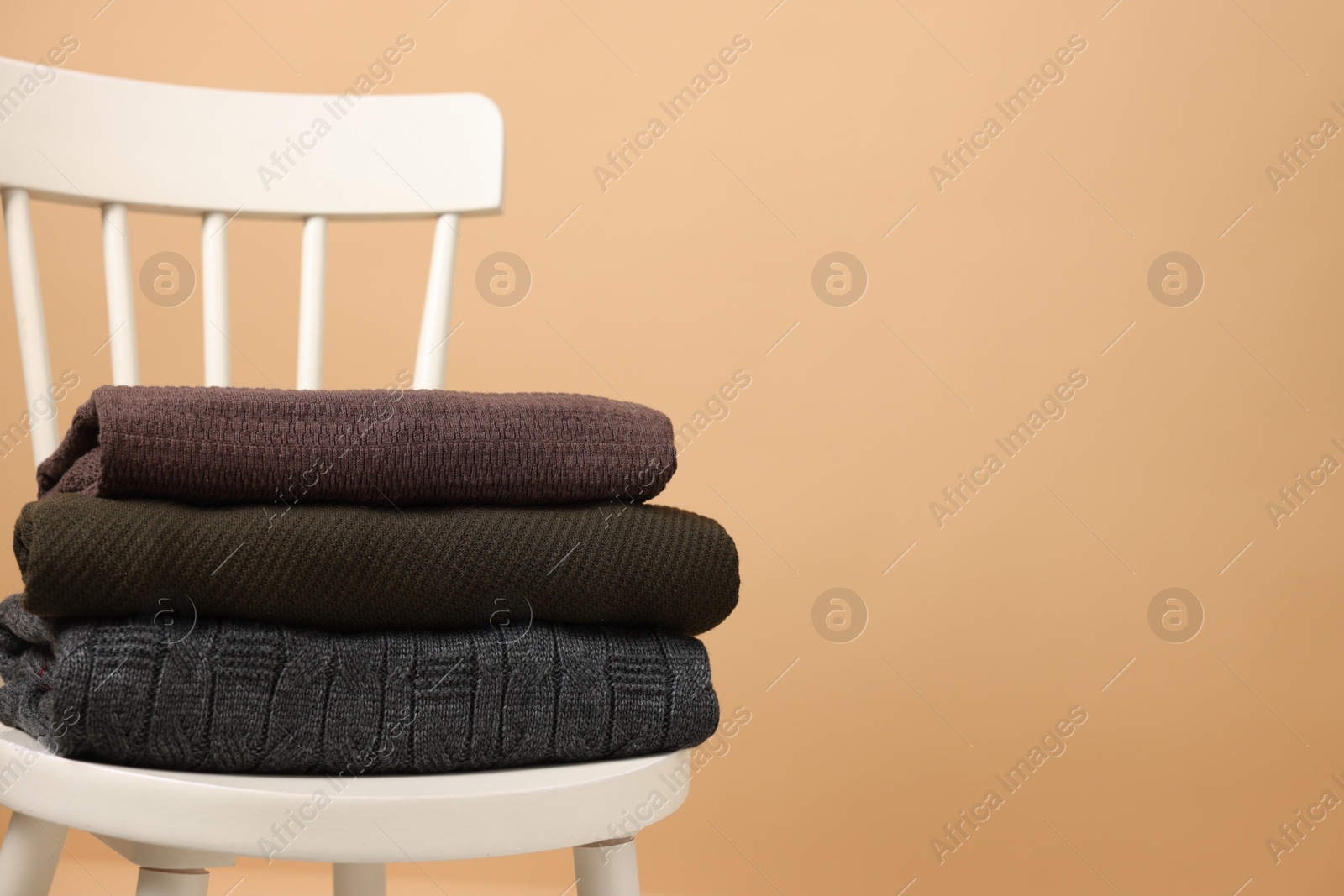 Photo of Stack of different warm sweaters on white chair against beige background. Space for text