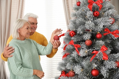 Happy mature couple decorating Christmas tree at home