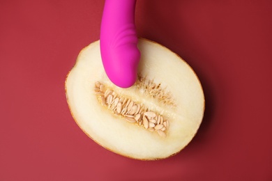 Photo of Half of melon and purple vibrator on red background, flat lay. Sex concept