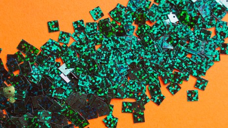 Many green sequins on orange background, flat lay