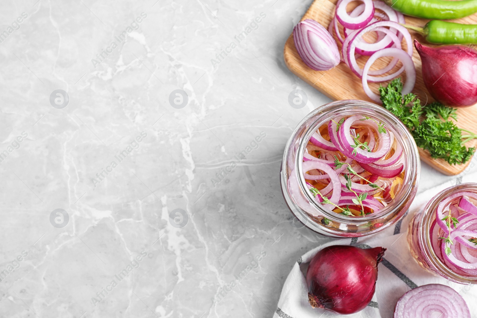 Photo of Flat lay composition with jars of pickled onions on marble table. Space for text