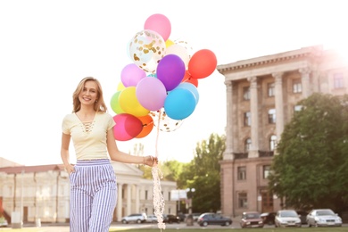 Young woman with colorful balloons outdoors on sunny day