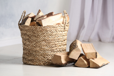 Wicker basket with cut firewood on white floor indoors
