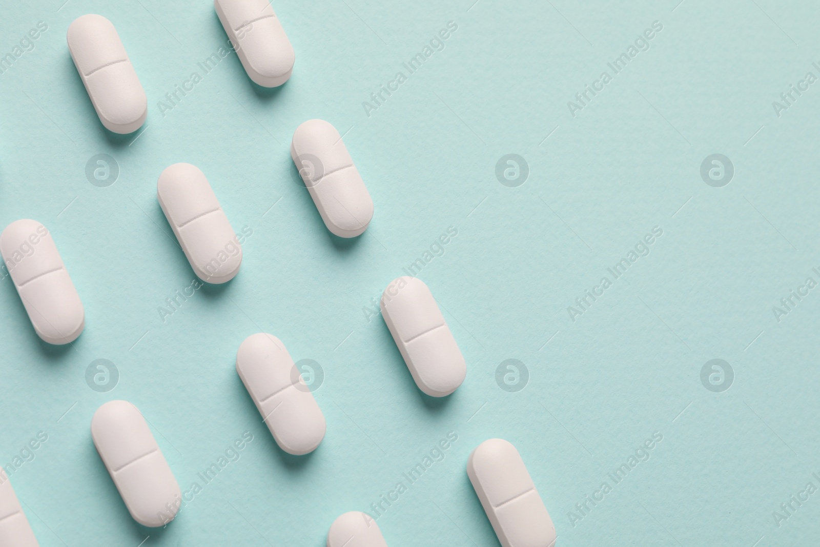Photo of White pills on mint background, flat lay. Space for text