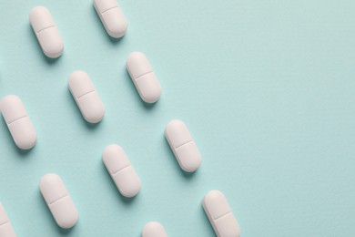 White pills on mint background, flat lay. Space for text