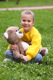 Photo of Little girl with teddy bear on green grass outdoors