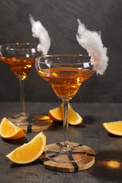 Photo of Tasty cocktails in glasses decorated with cotton candy and orange slices on gray table