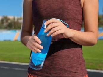 Photo of Sporty woman holding bottle of water at stadium on sunny day, closeup