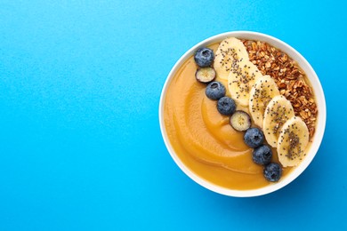 Delicious smoothie bowl with fresh blueberries, banana and granola on light blue background, top view. Space for text