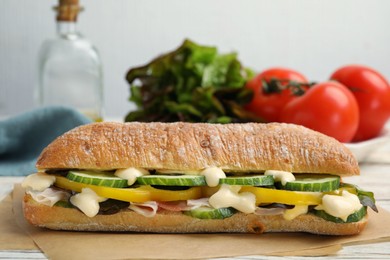 Photo of Delicious sandwich with vegetables, ham and mayonnaise on parchment paper, closeup