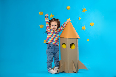 Photo of Little child playing with rocket made of cardboard box near stars on blue background